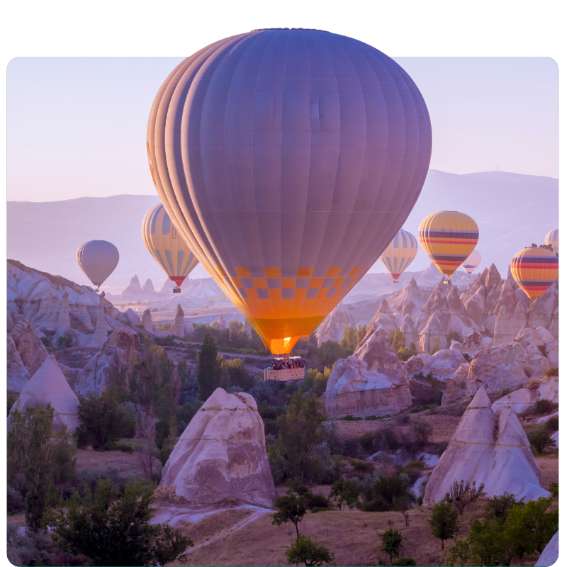 Hot air balloons drift above a scenic landscape with rocky formations and sparse greenery, resembling the careful balance required in financial planning. The clear sky, tinged with a soft purple hue, creates a tranquil atmosphere perfect for reflection on future goals.